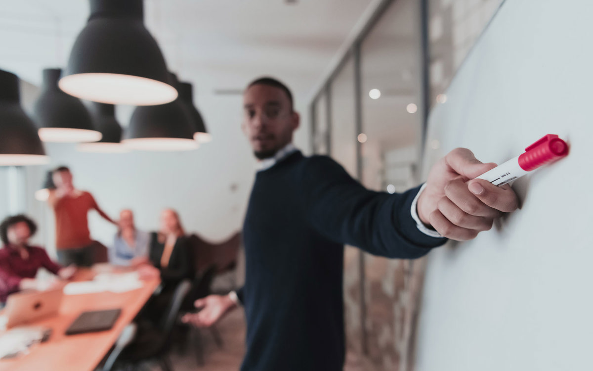 training man presenting from whiteboard to blurred class