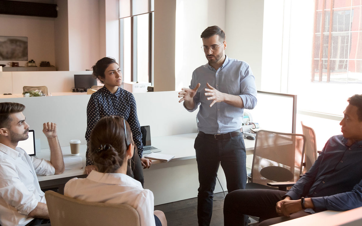 training man standing talking to 4 sitting others