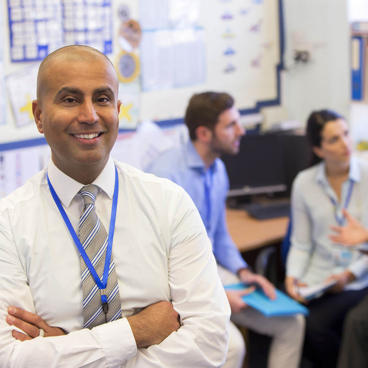 teacher smiling whilst a meeting is being conducted behind him