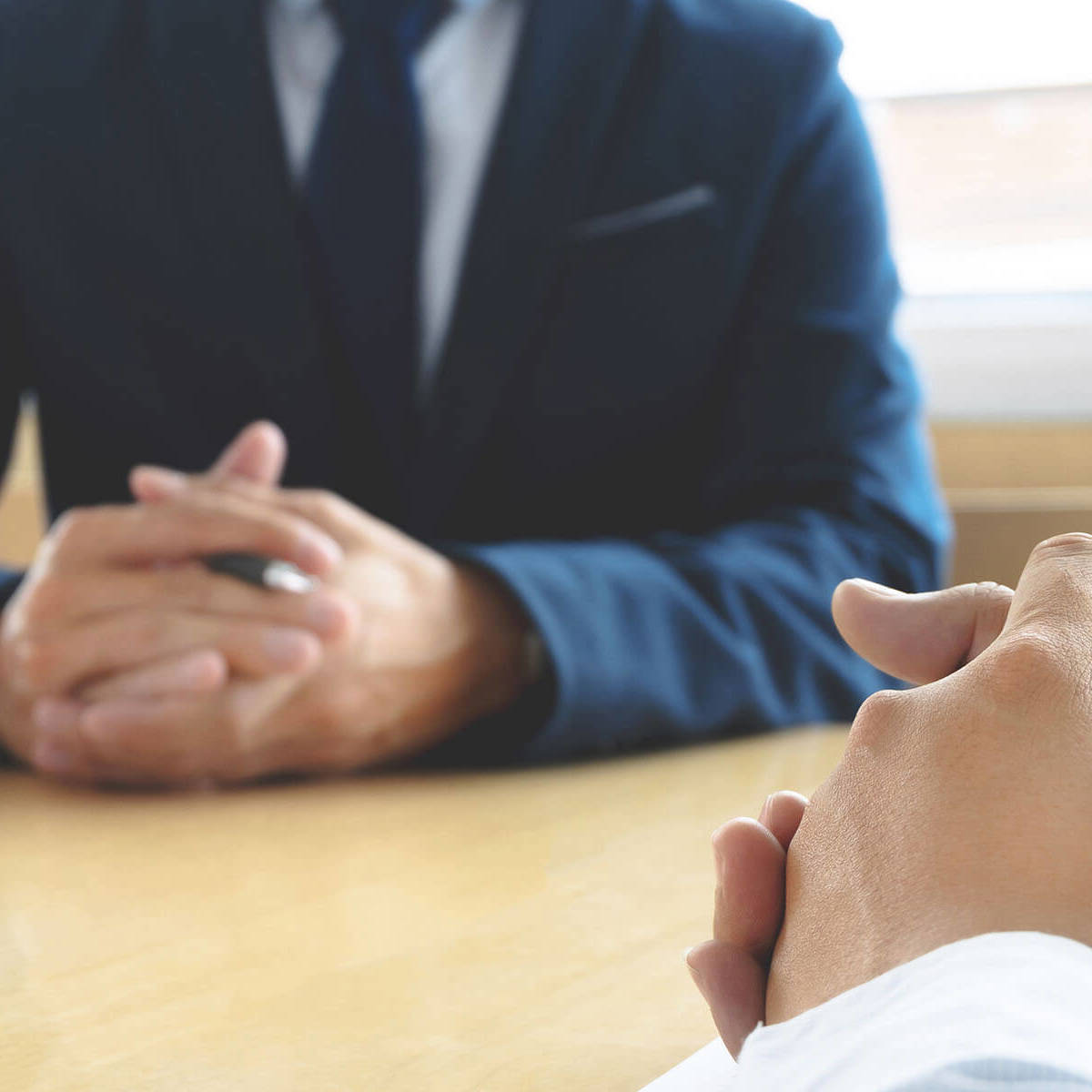 man with his hands clenched together sitting at a meeting