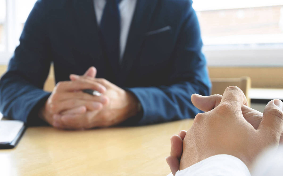 man with his hands clenched together sitting at a meeting