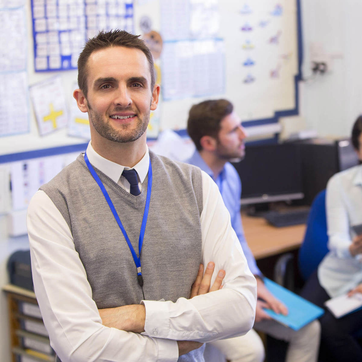 people teacher smiling into the camera with other teachers talking to each other behind him