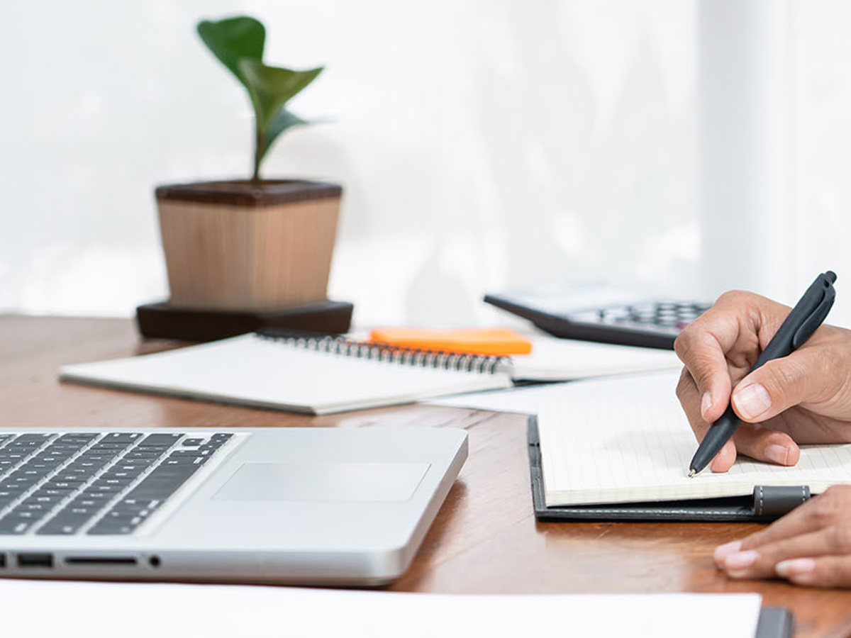 training woman at desk writing notes from her laptop