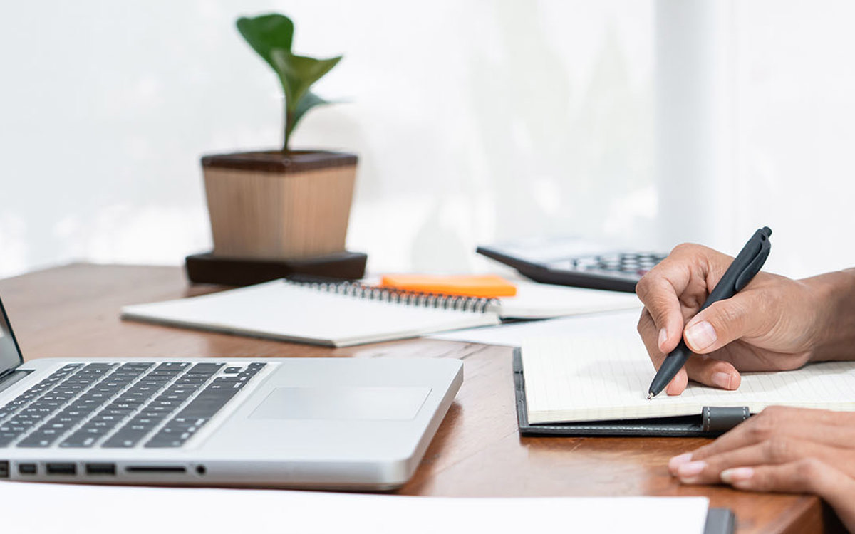 training woman at desk writing notes from her laptop