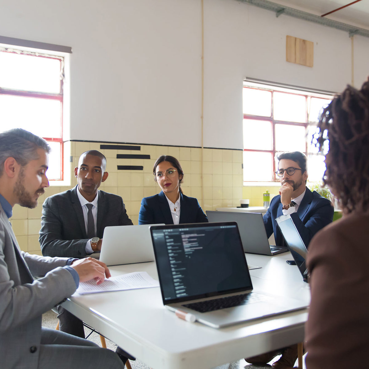 training group of five professionals sitting at a table with laptops