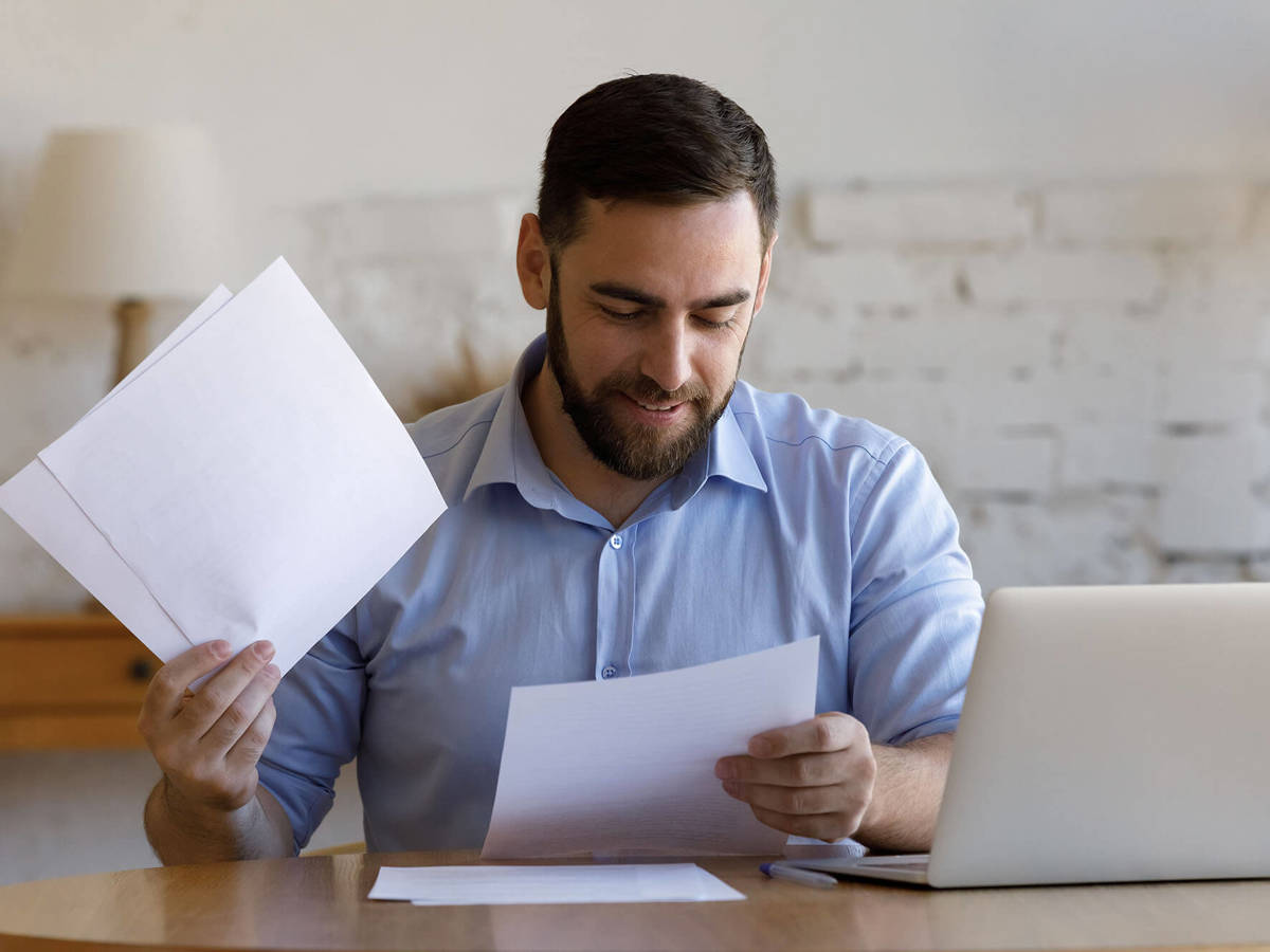 tools-resources man checking over pieces of paper with laptop beside him